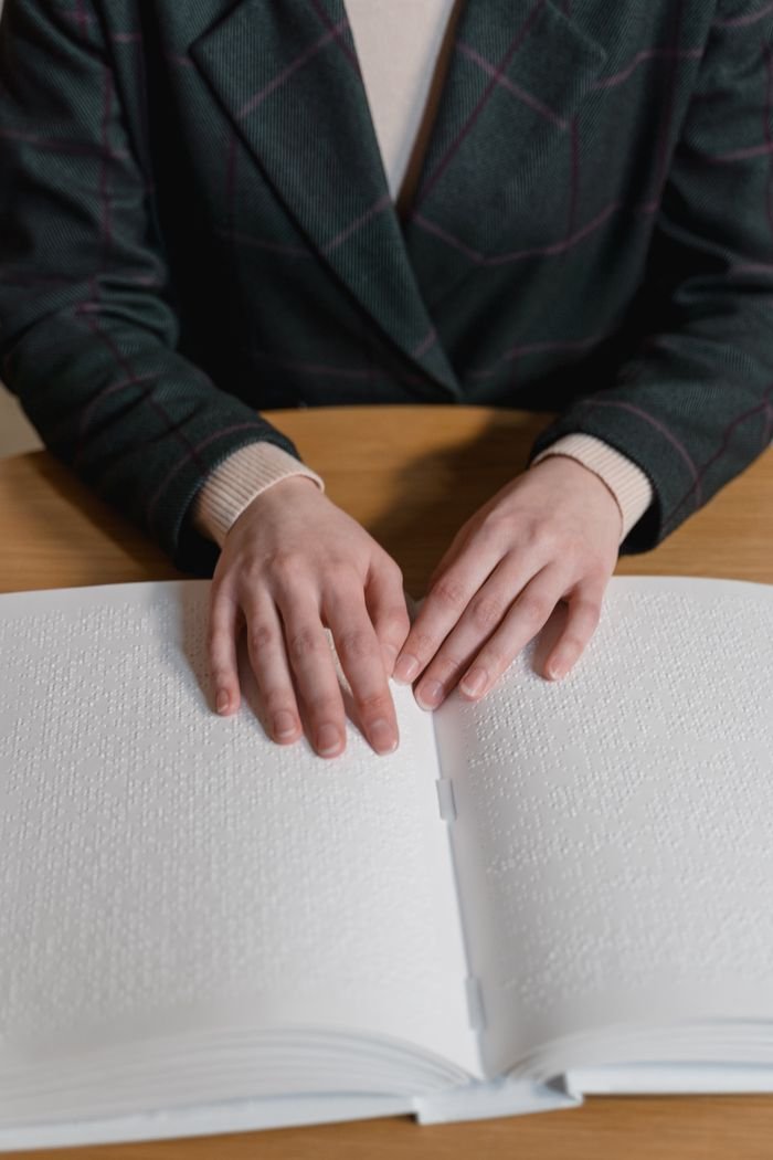 Services A person reading Braille, focusing on hands and book for visually impaired education.