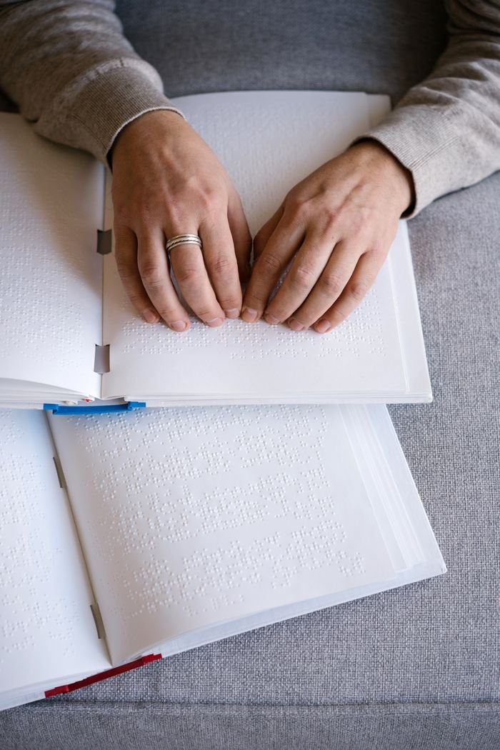 Services Hands reading Braille text on an open book, representing tactile reading and accessibility.