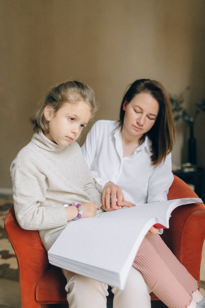 Services A mother guides her daughter through a braille book, promoting inclusive education.