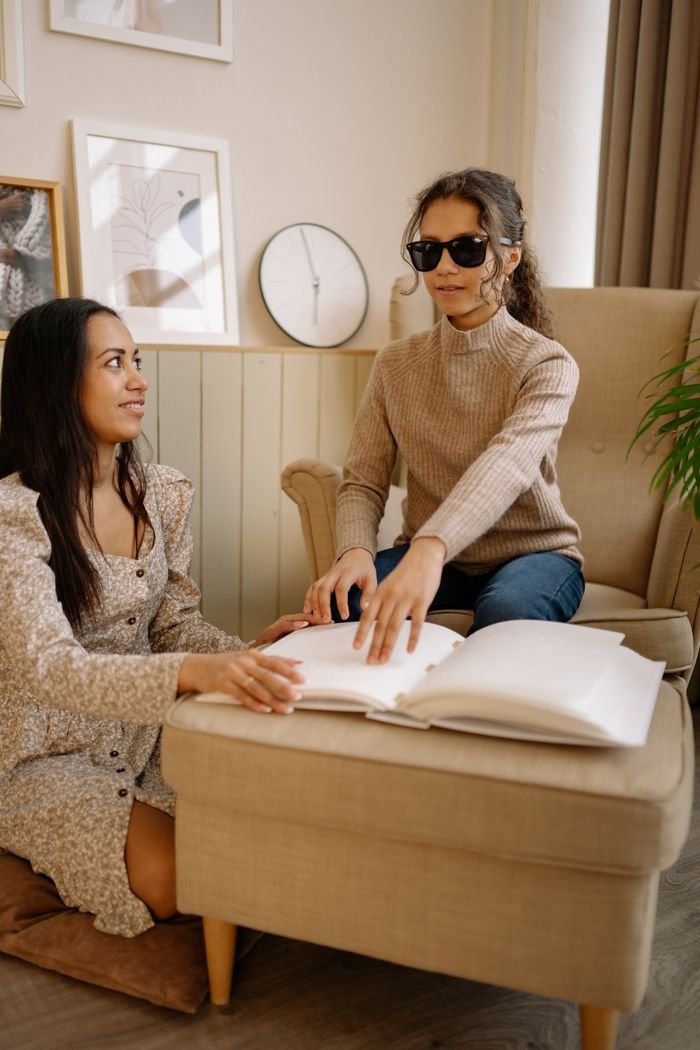 Services Two women engage in Braille reading session indoors, highlighting inclusivity and education.