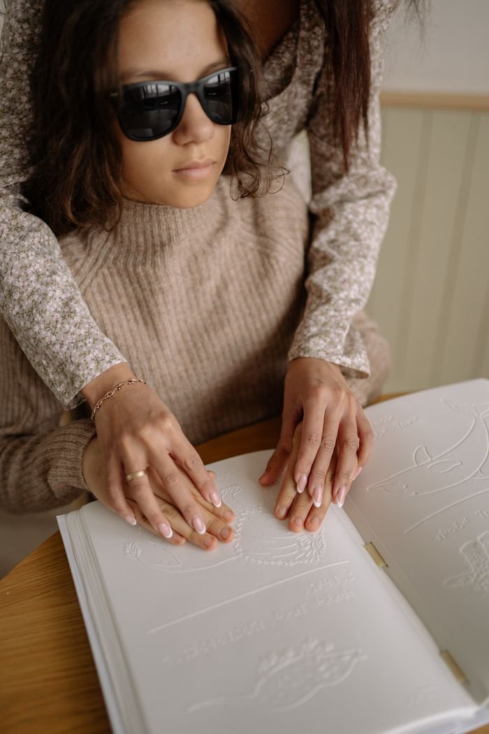 Services A child reading Braille with adult guidance, depicting education and support.