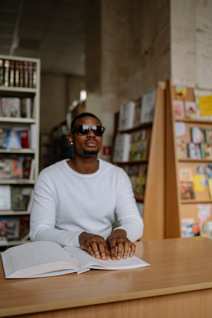 Services African American man reading Braille in a library, representing disability awareness.